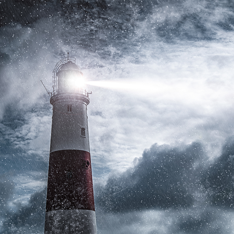 Large red and white lighthouse on a rain and storm filled night with a beam of light shining out to sea